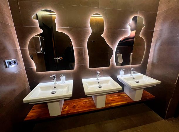 imagen de tres espejos con formas de personas encima de los lavabos con luces para el baño seguramente de chicos